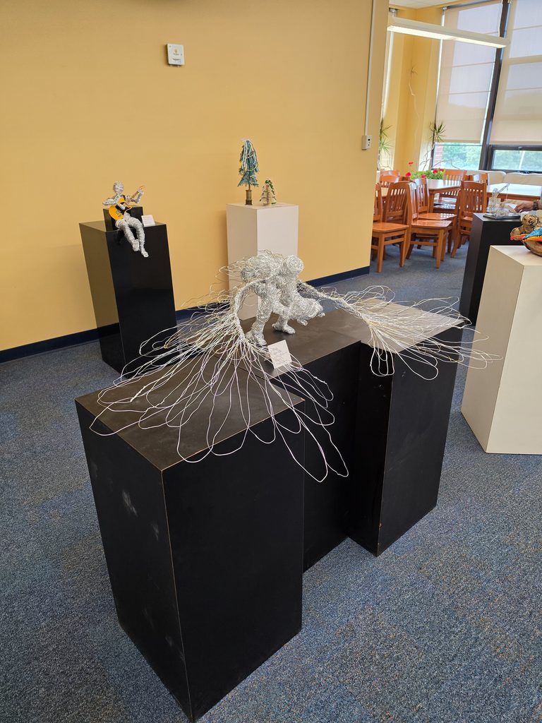 Photo of a sculpture of a crouching angel-like creature with large wings. Made from wrapped wire.