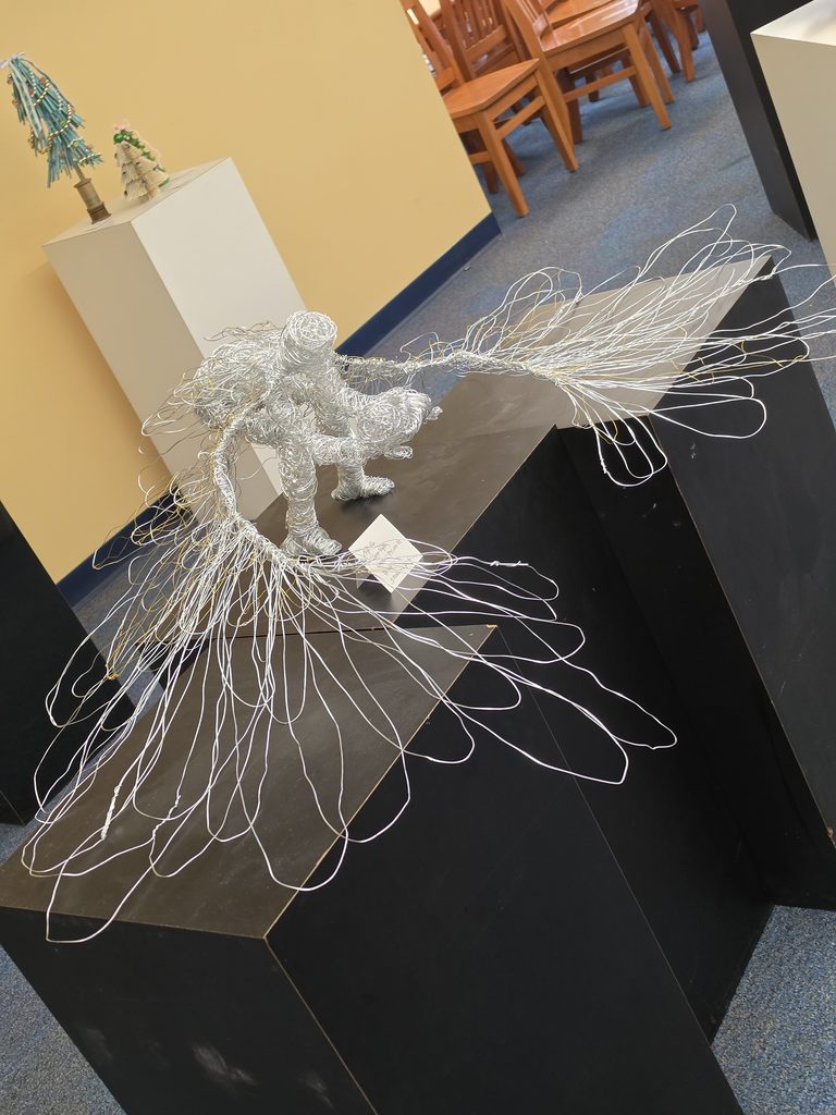 Photo of a sculpture of a crouching angel-like creature with large wings. Made from wrapped wire.